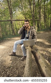 Busy Young Environmentalist Is Talking On The Phone While Working On Laptop In The Woods