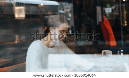 busy young girl student in a white jacket and wearing glasses sitting in a cafe after studying
