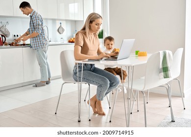 Busy Young Mother Working From Home Office Using Laptop Computer Sitting At Kitchen Table With Cute Kid Child Son At Home While Dad Cooking. Parents And Child, Distance Virtual Work In Family Life.