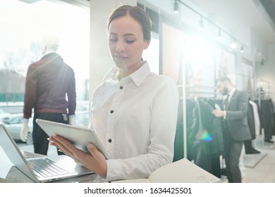 Busy Young Sales Consultant Of Clothing Store Using Digital Tablet While Checking Goods In Online Catalogue