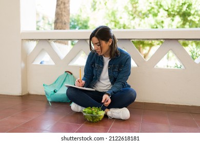 Busy Young Woman Doing Homework On The College Campus While Eating Lunch Before Attending A Class