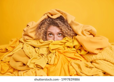 Busy Young Woman Has Overflowing Closet With Outdated Clothes Focused Above Covered By Huge Stack Of Yellow Apparels Thinks About Recycling. Disorder And Mess In Wardrobe. Fast Fashion Concept