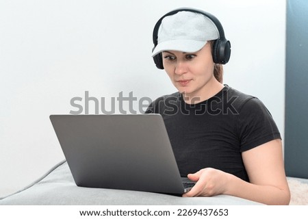 Busy young woman in headphones working on laptop, making video call and looking at laptop screen with positive emotions, online work and online communication, copy space and white background.