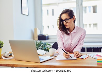 Arbeitskräftige junge Frau, die im Büro mit Dokumenten und Laptop arbeitet
