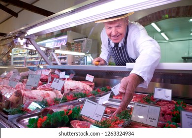 Butcher in apron and hat arranging display of meat in shop chiller