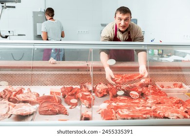 Butcher in an apron offers to buy fresh meat in the grocery store section - Powered by Shutterstock