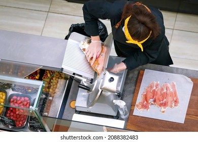 Butcher cut prosciutto, slicing prosciutto on cutting machine. View from above on female butcher cutting meat at butcher counter. Selective focus - Powered by Shutterstock