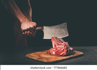 Butcher Cutting Raw Meat With Cleaver On Wooden Cutting Board