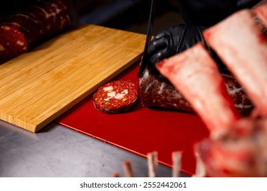 Butcher hands that slicing of homemade sausage on a wooden cutiing board along with pork. Butchers table with sausage and ribs. - Powered by Shutterstock