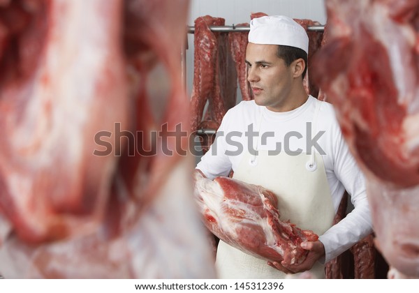 Butcher holding\
slab of meat in the meat\
locker