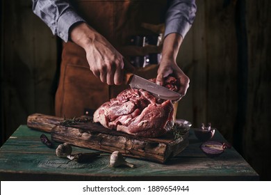 A Butcher In A Leather Apron Cuts A Large Piece Of Meat On A Wooden Board.