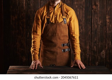 Butcher On A Wooden Background In A Leather Apron.