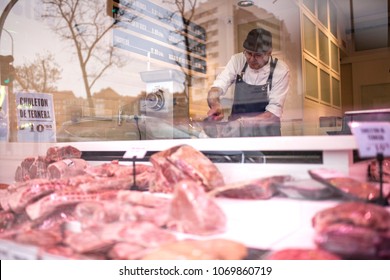 Butcher serving customers seen through the storefront