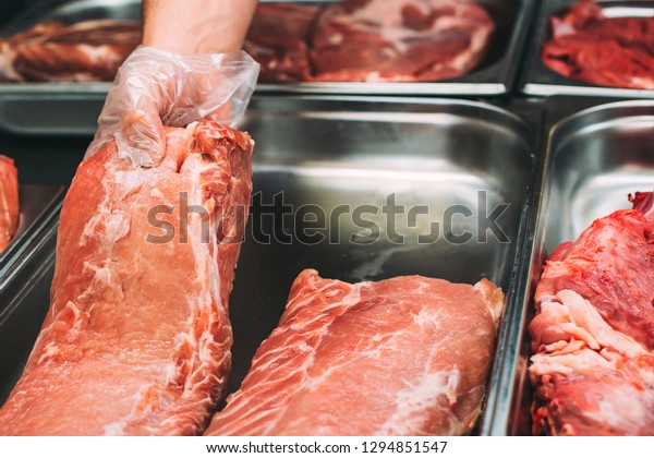 Butcher shop. Butcher\'s hands holding meat piece\
in shop. Best offer of fresh meat at display in supermarket. Raw\
beef and pork in meat shop. Raw meat in assortment. Fresh pork at\
market