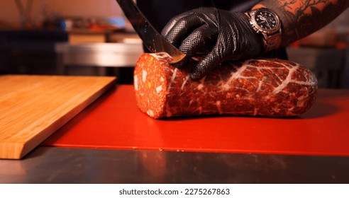 Butcher slicing handmade sausage in a butchers kitchen. Male hands placing a sausage on the cutting table. - Powered by Shutterstock