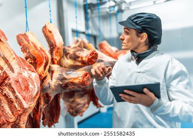 Butcher using technology in a innovative meat processing factory checking the meat using digital tablet - Powered by Shutterstock