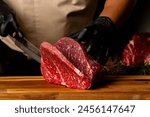 The butcher wearing black gloves cuts the meat with knife on wooden cutting board.Close-up piece of raw meat with a chef