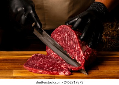 The butcher wearing black gloves cuts the meat with knife on wooden cutting board.Close-up piece of raw meat with a chef's knife on a dark background. - Powered by Shutterstock