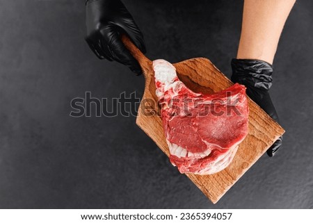Butcher woman prepare fresh raw meat pork entrecote steak on wooden board, top view on dark background.