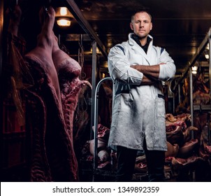 The butcher in workwear with his arms crossed in a refrigerated warehouse in the midst of meat carcasses - Powered by Shutterstock