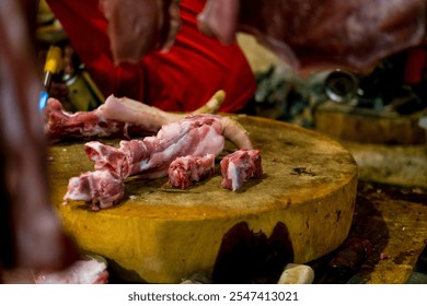 At a butcher's stall, a large piece of pork is being cleaned with a torch in the background, while another piece sits on a wooden cutting board in the foreground. Selective focus photo - Powered by Shutterstock