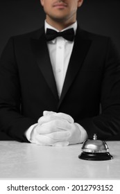 Butler at desk with service bell against black background, closeup view