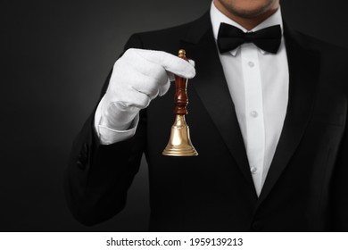 Butler holding hand bell on black background, closeup