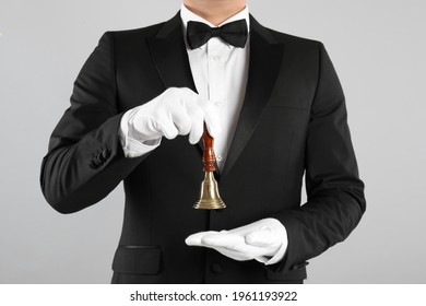 Butler holding hand bell on grey background, closeup