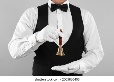 Butler holding hand bell on grey background, closeup
