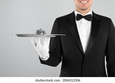 Butler holding metal tray with service bell on grey background, closeup