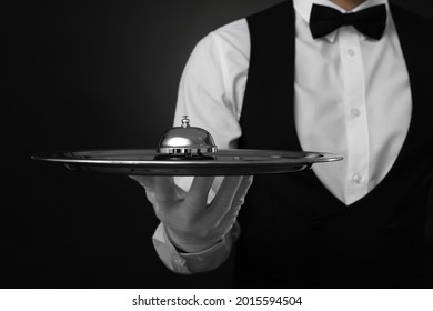 Butler holding metal tray with service bell on black background, closeup