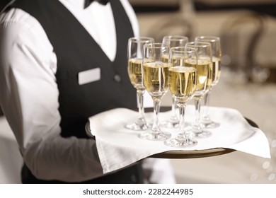 Butler holding tray with glasses of sparkling wine in restaurant, closeup