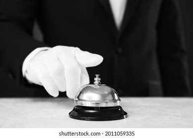 Butler ringing service bell at table on black background, closeup