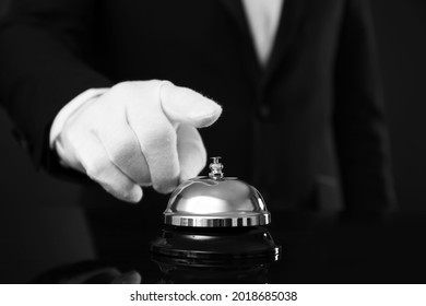 Butler ringing service bell at table on black background, closeup