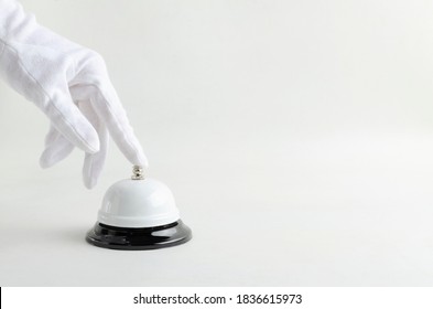 Butler wearing white glove and ringing service bell, bright background.Empty space