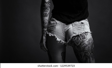 Butt close up of sexy woman wearing short jeans and tattoos against dark background. Black and white image with film grain.