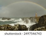 Butt of Lewis lighthouse with crashing white waves dark skies cliffs rocks and a rainbow.