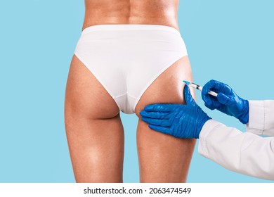 Butt Lifting Concept. Rear back view of slim woman having hip injection at beauty salon, closeup. Plastic surgeon making injection at buttocks area for unrecognizable lady, blue studio background