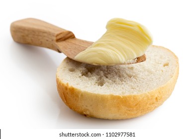 Butter On Wooden Knife Resting On Half Of Crusty Bread Roll Isolated On White.