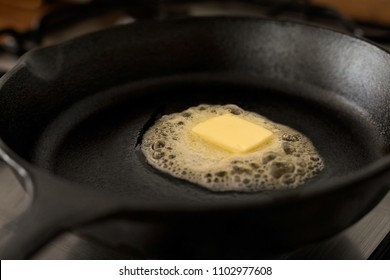 A Butter Pat Melting On A Black Cast Iron Frying Pan.