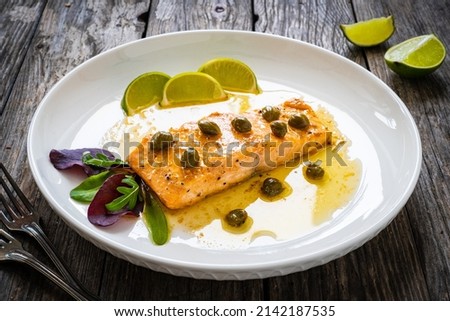 Butter sauce fried salmon steak with capers and lime on wooden table 