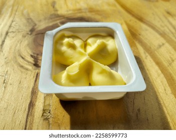 Butter in a white plastic container on the top of wooden table. A single serve pack - Shutterstock ID 2258599773