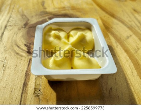 Butter in a white plastic container on the top of wooden table. A single serve pack