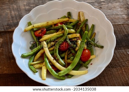 Buttered string beans sauteed with garlic and tomatoes organically grown in a white dish on a farm table.