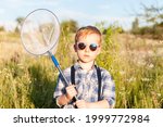 Butterfly hunter - little cute boy wearing sunglass and holding bug net in the hands, standing in the meadow