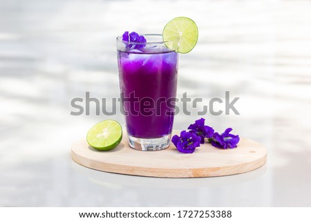 Butterfly pea juice with ice in transparent cup serve on Wooden sheet with flower and lemon (Clitoria ternatea). White background clipping path. 