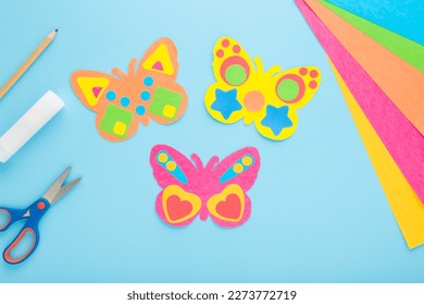 Butterfly shapes from colorful paper on light blue table background. Pastel color. Making decoration elements. Closeup. Top view. - Powered by Shutterstock