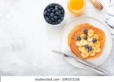 Buttermilk Pancakes with banana, blueberries and honey on concrete background. Top view and copy space for text. Top view of pancakes with berries on table