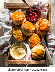 Buttermilk scones with a jar of cream and strawberry jam are sweet and delicious on a wooden board with a knife
				