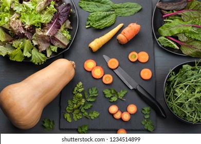 Butternut Squash, Carrots, Mixed Leafy Greens, Cilantro And Sorrel In A Kitchen Scene With Dark Background.